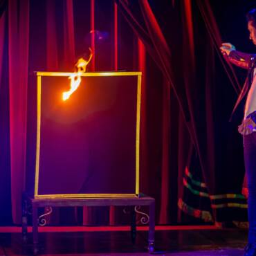 Rodrigo, mago del Circo Raluy Legacy, haciendo magia con fuego y un cuadro con marco dorado.
